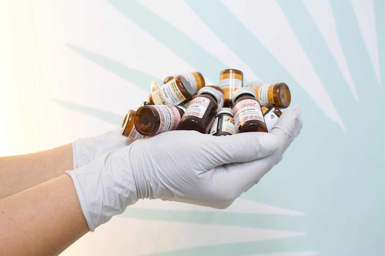ours-journey A close-up of gloved hands holding multiple medicine bottles against a light background.