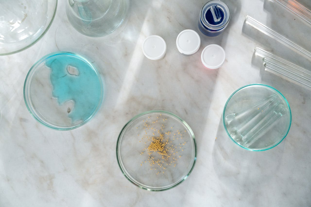about-img A top-down view of petri dishes and lab equipment on marble with blue liquid and golden particles.